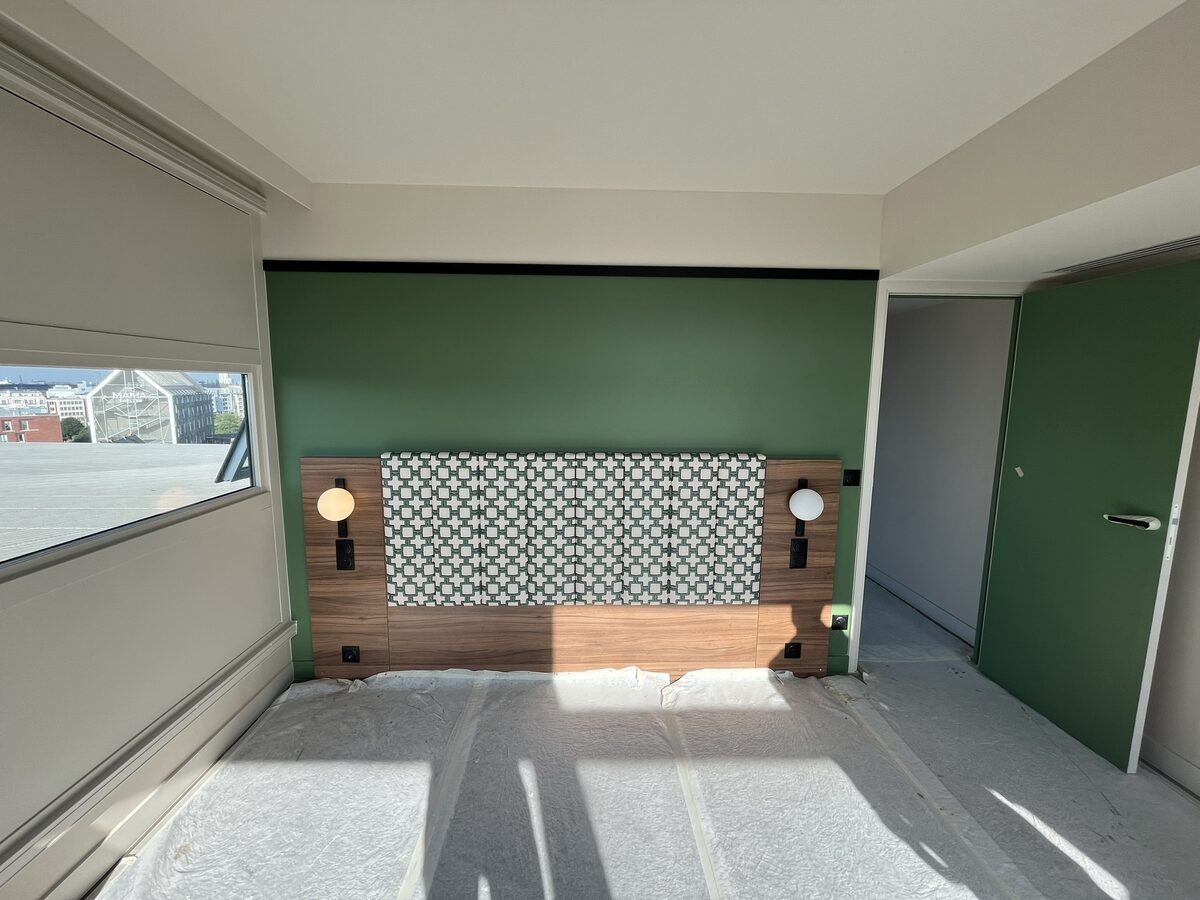 Chambre d'aparthotel livrée — mur d'accent vert et tête de lit sur mesure